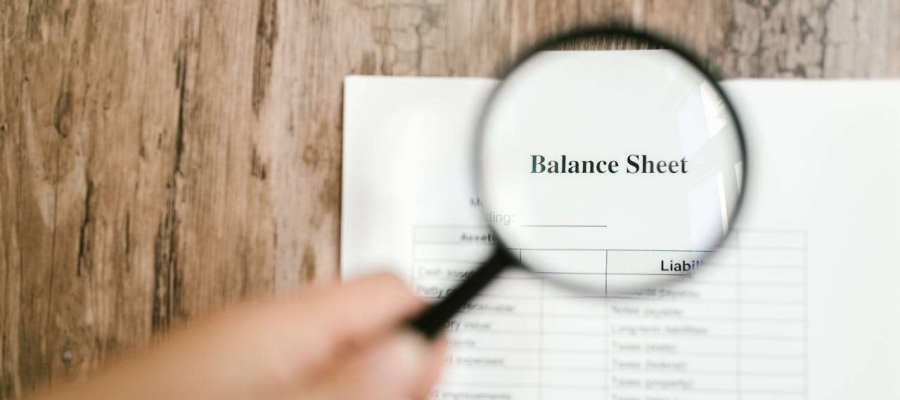 an image showing a balance sheet being looked a via a magnifying glass