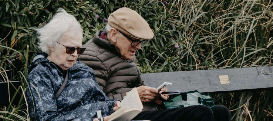 two elderly people sitting on a bench outside.