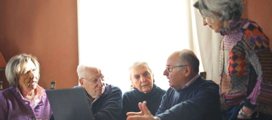 a group of elderly people having a discussion in front of a laptop