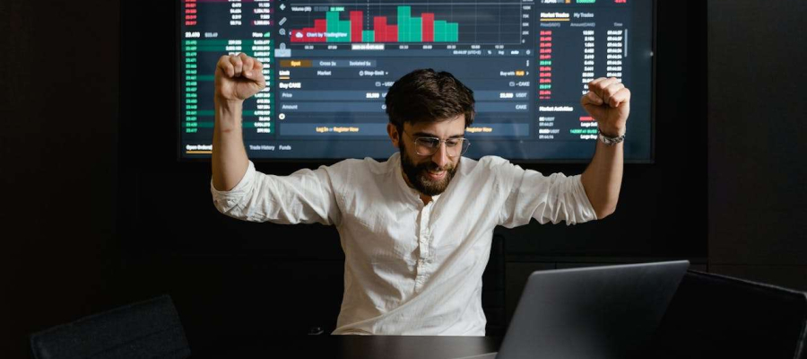 a man sitting in front of investment charts looking at a laptop. The man is happy.