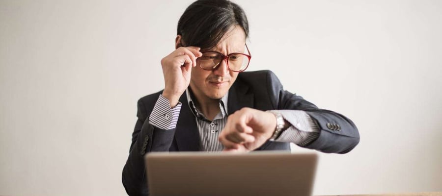 a man sitting at a laptop checking his watch for the time