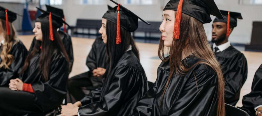 a group of students sitting in a hall with graduation gowns