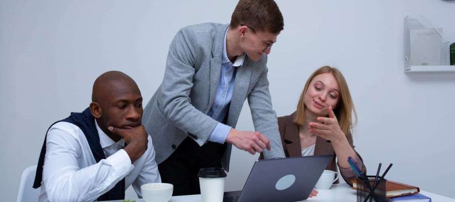 three people sitting at a table looking at a laptop and discussing