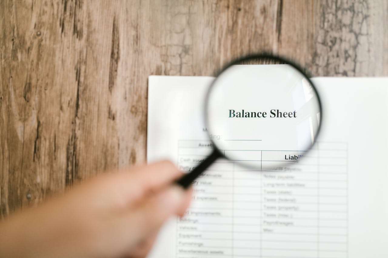 an image showing a balance sheet being looked a via a magnifying glass