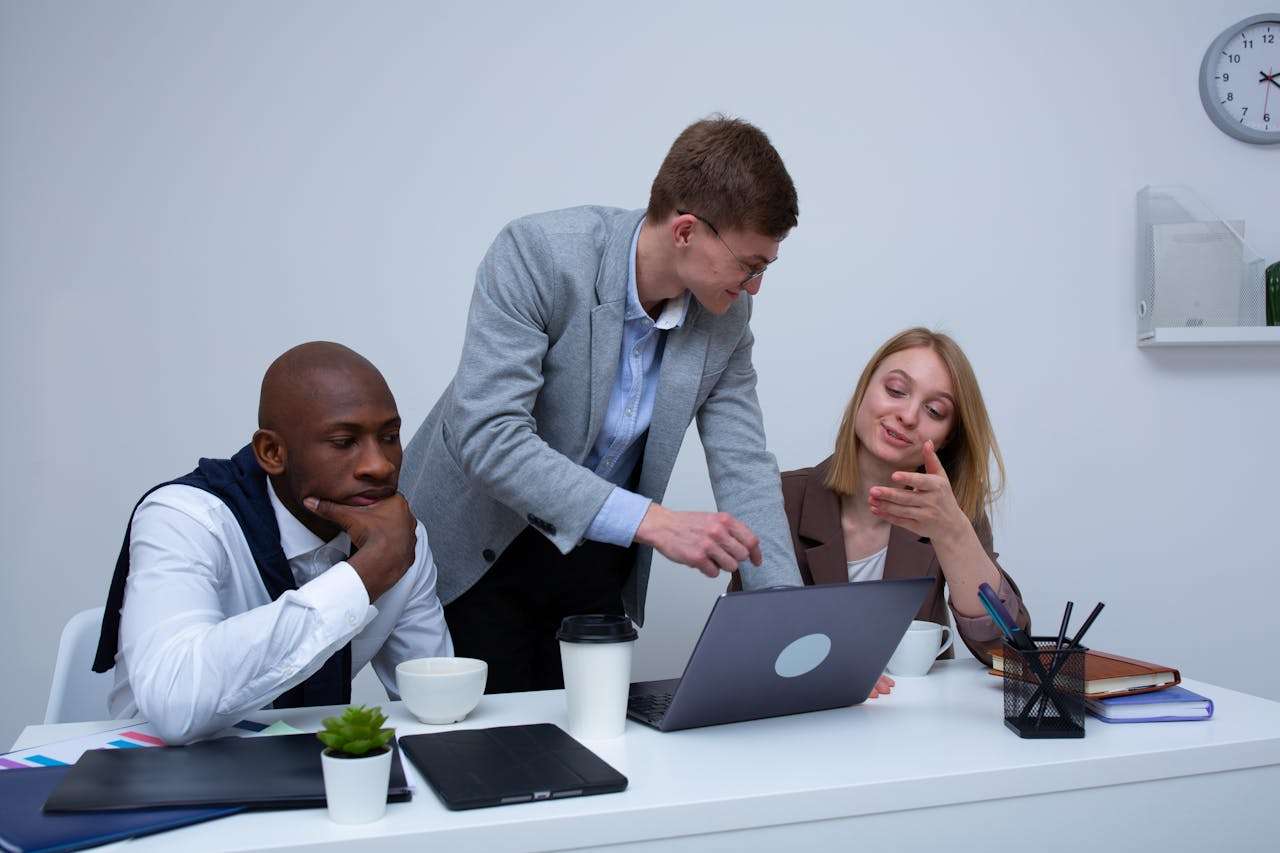 three people sitting at a table looking at a laptop and discussing