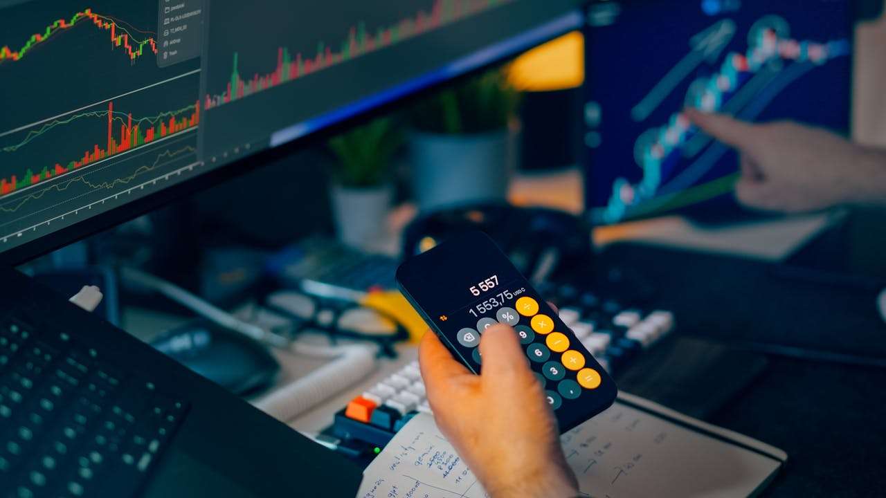 a person looking at stock charts and using a phone to calculate prices