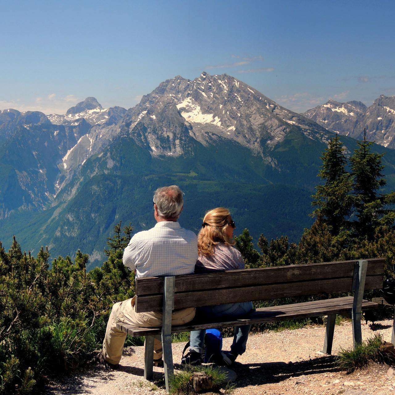 a couple sitting on a bench in front of a mountain