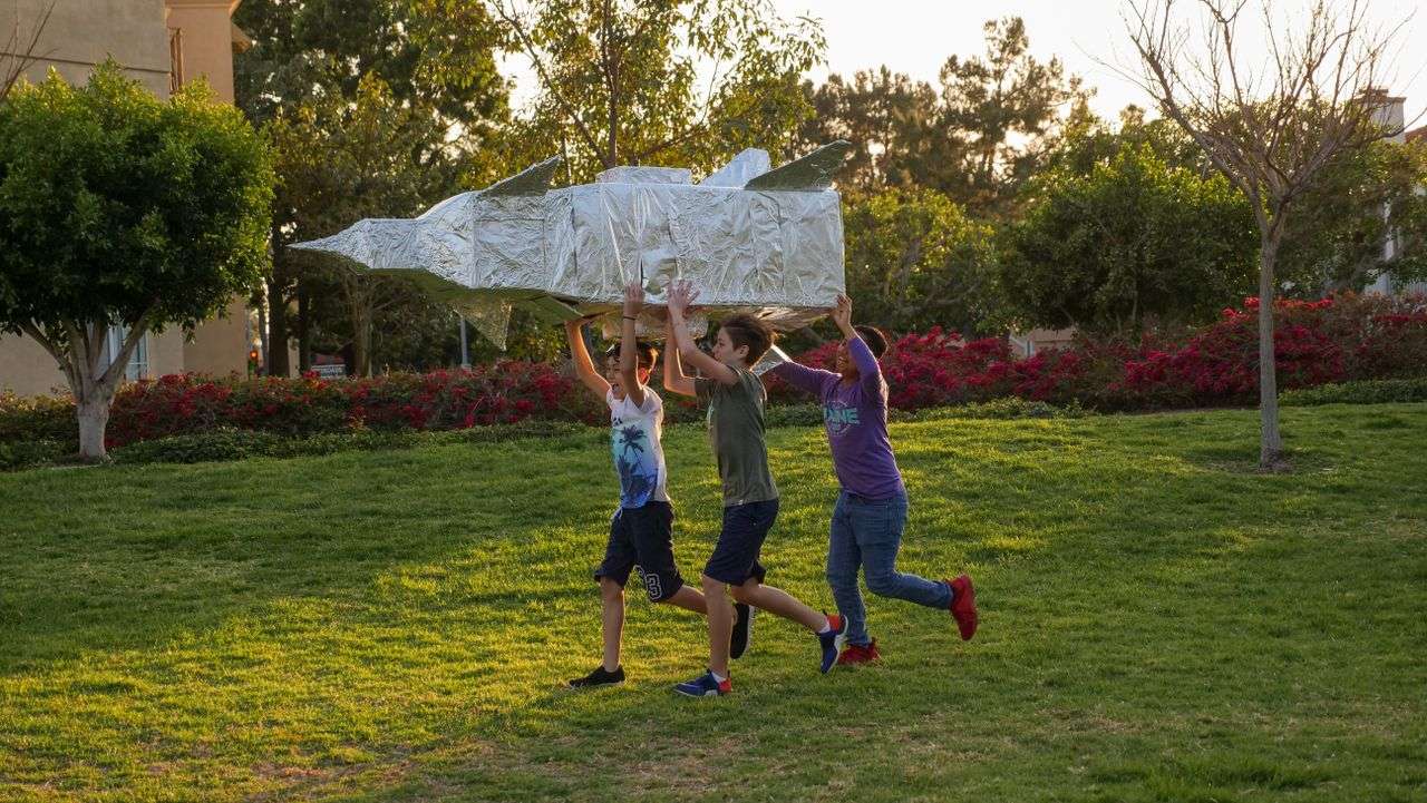 kids holding a rocket ship running across the yard