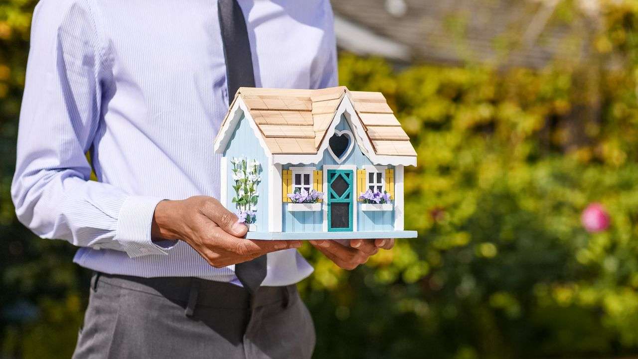 a man holding a small house to represent a mortgage